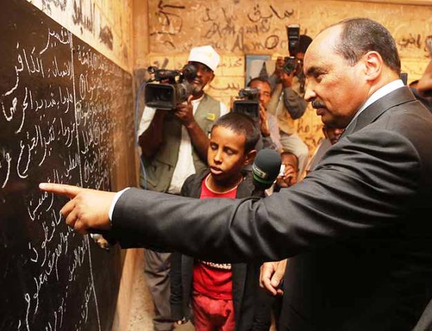 الرئيس الموريتاني محمد ولد عبد العزيز وهو يزور مدرسة كوميز المكتظة بالطلاب والتي تظهر في الصورة حجراتها متسخة الجدران وتملؤها الشعارات والعبارات المكتوبةة (وم أ)